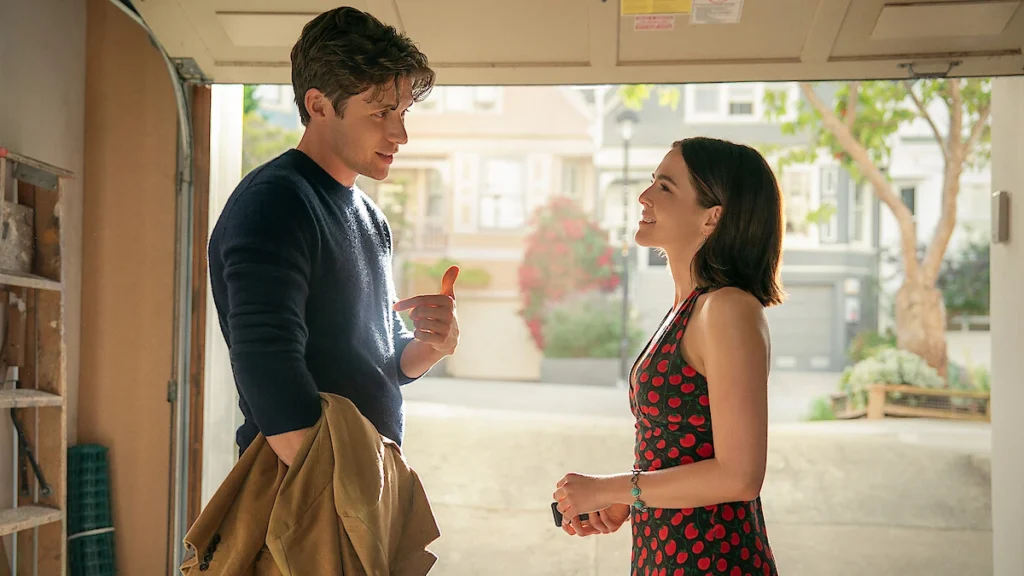 Nick Robinson as Wes and Zoey Deutch as Jill standing under an open garage door, smiling and looking at each other in a scene from Voicemails for Isabelle