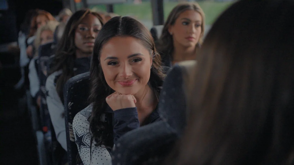 Dallas Cowboys Cheerleader Reece sits on the team bus smiling in their warm-up gear during America's Sweethearts Season 3 on Netflix