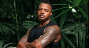 A close-up portrait of Wes Saunders, a cast member of Outlast: The Jungle (Season 3), standing with his arms crossed and staring at the camera