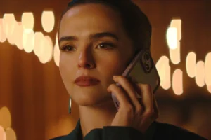 Close-up of Zoey Deutch as Jill looking emotional while listening to a phone call in Netflix's Voicemails for Isabelle, against a warm bokeh background of lights