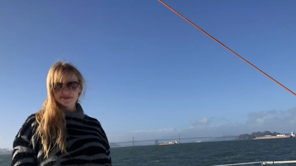 Caroline Joanne Herrling wearing sunglasses and a striped sweater on a boat in the San Francisco Bay, with a bridge visible in the background