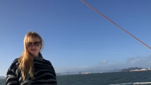 Caroline Joanne Herrling wearing sunglasses and a striped sweater on a boat in the San Francisco Bay, with a bridge visible in the background