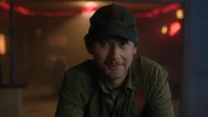 Dillard wearing a baseball cap and smiling in a dimly lit bar in The Walking Dead Dead City Season 3